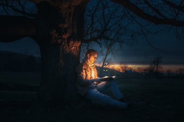 A man reading a book under a tree at night.