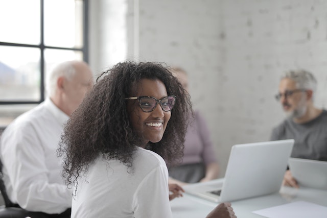 Smiling girl in glasses with her colleagues in the background.