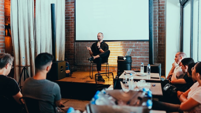 A male speaker engages with people in the audience.