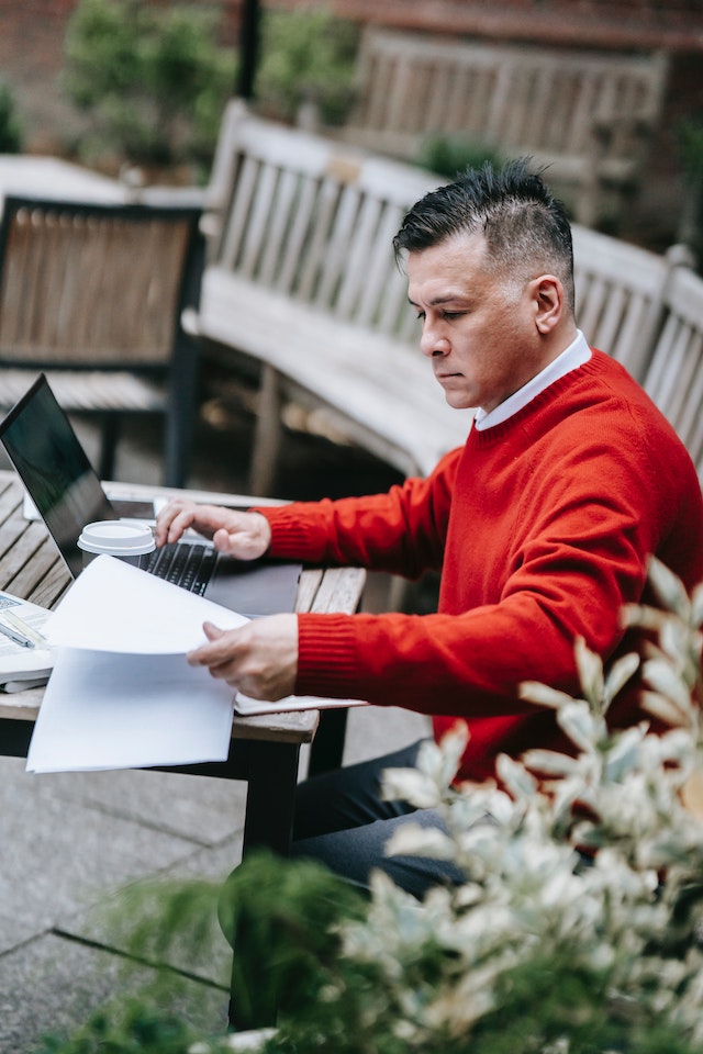 A guy working on his laptop while poring over some documents.