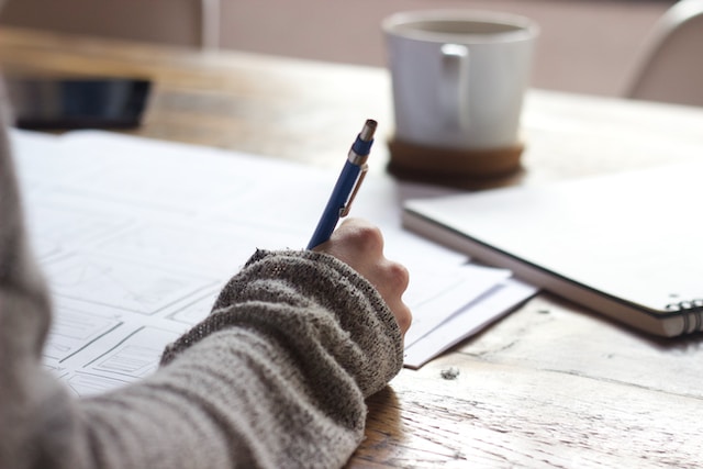 A hand holding a pen, writing on papers.