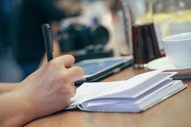 A hand holding a pen, writing on the pages of a notebook