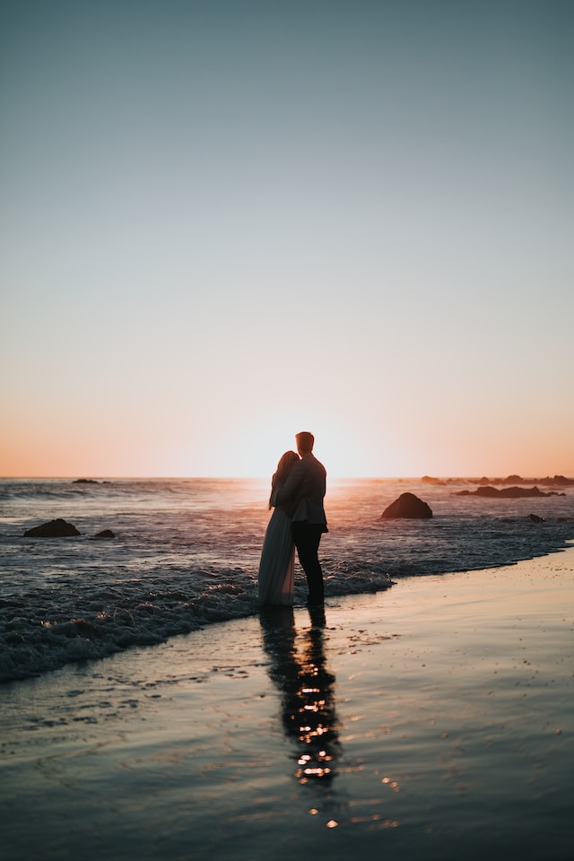 A couple standing on the shore watching the sunset