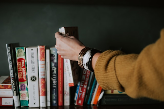 Person picking out a book from a bookshelf