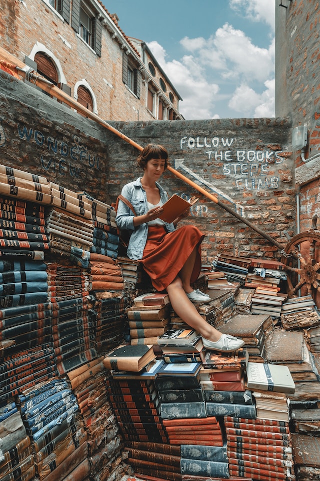 A woman sitting on piles of books while reading one