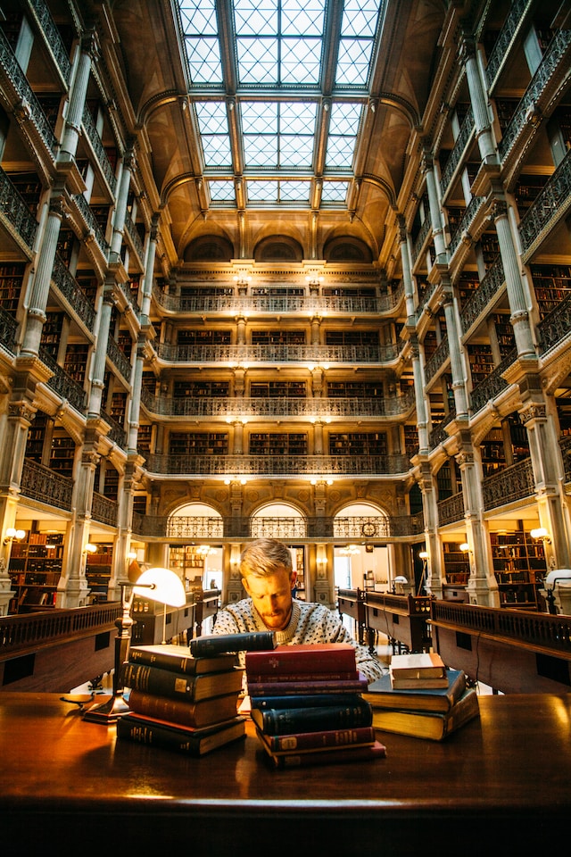 Person with stacks of books on his table inside a library