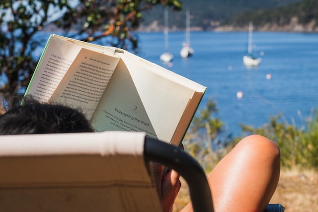 Person reading a book on a chair overlooking the sea
