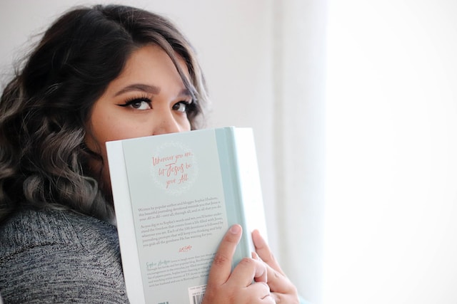 Woman peeking from the page of an open book she is holding 