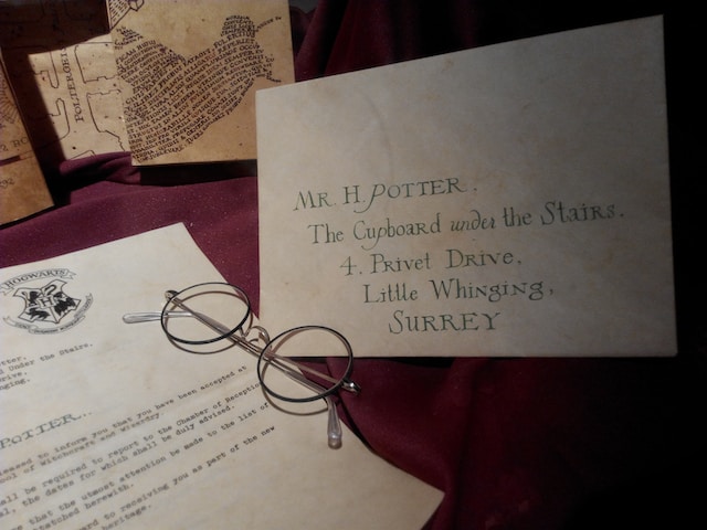 An open letter, an envelope with and address and a pair of glasses on top of a purplish-red fabric