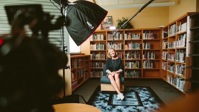 A woman being filmed with bookshelves behind here 