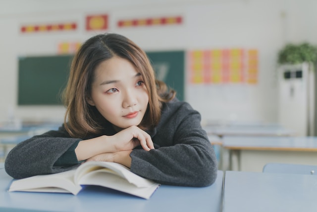 Woman leaning over an open book while looking outside