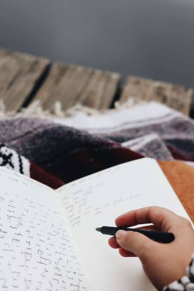 Person holding a black pen and writing on a notepad