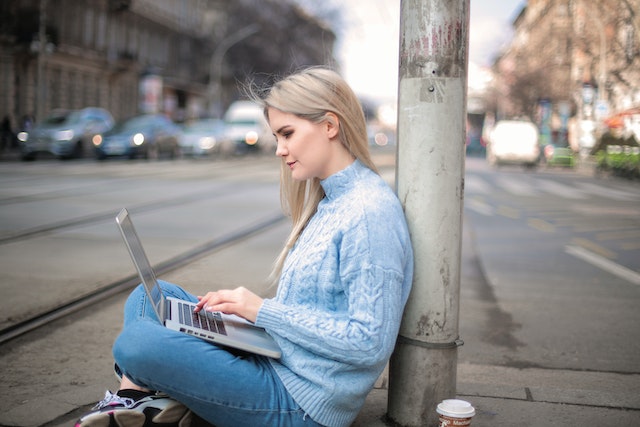 Woman in blue shirt working on her laptop while sat on the pavement