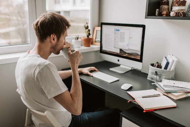 Gu in white shirt sipping on a cup of coffee while staring at the computer screen