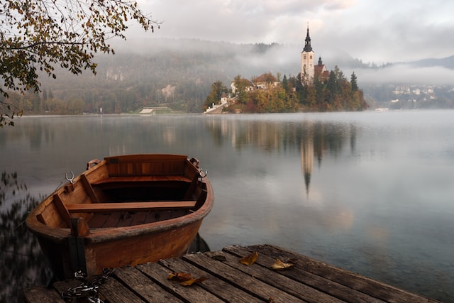 A boat next to w wooden dock next to a still lake with a castle in the middle